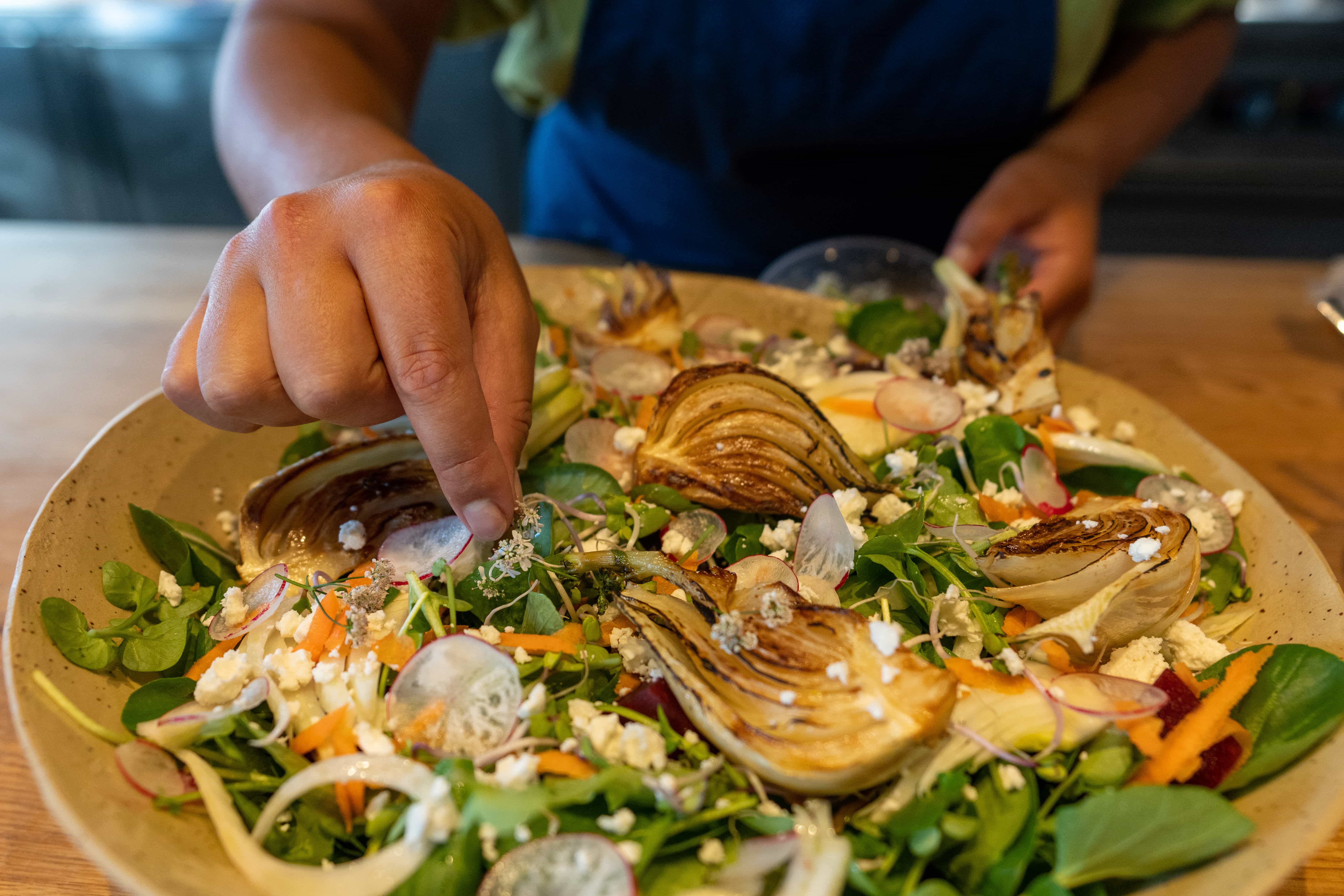 Onze chef legt de laatste garnering op een bord met geroosterde venkel, radijs en feta